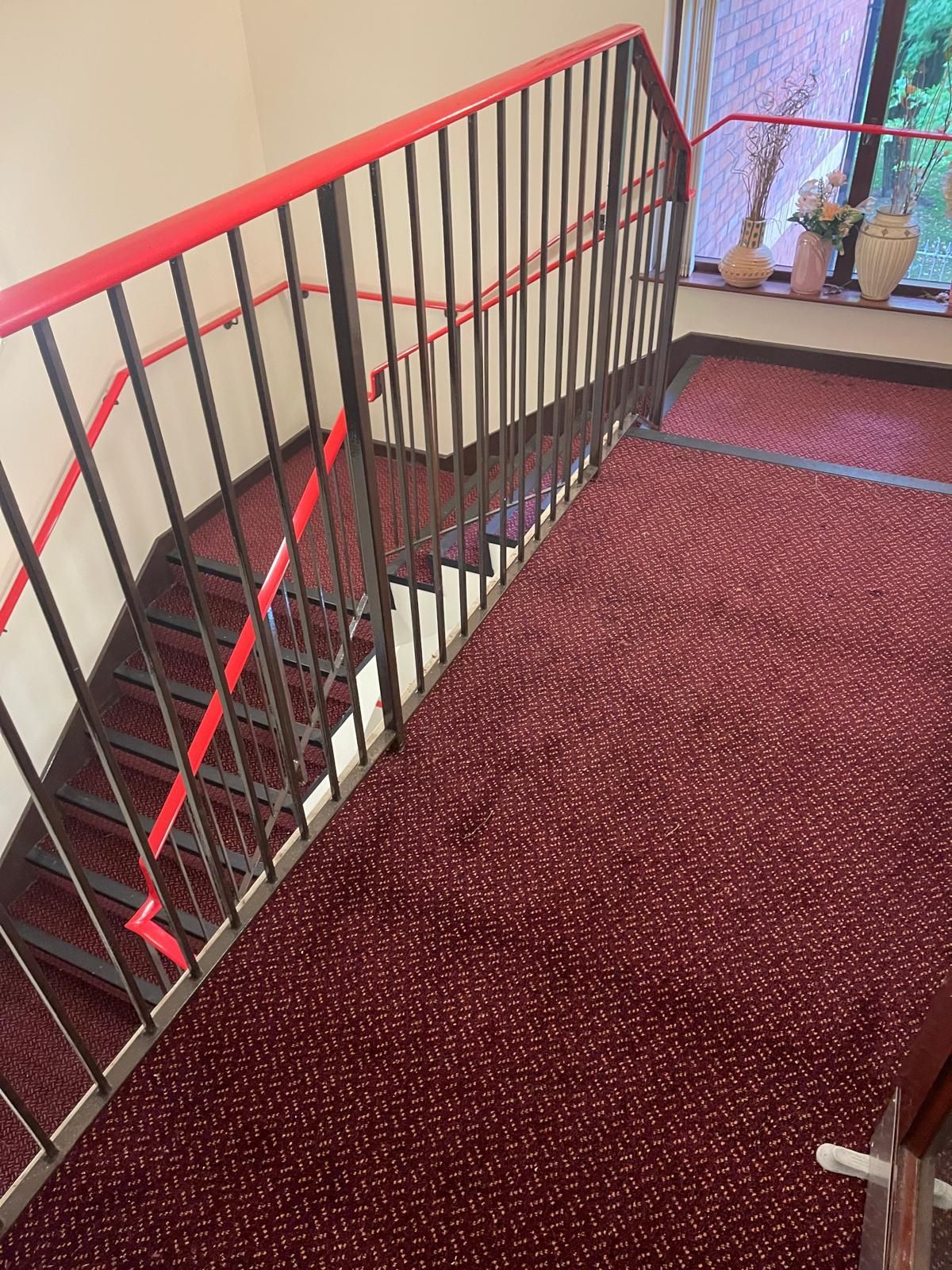 Staircase with red carpet and red handrails, black metal railings.