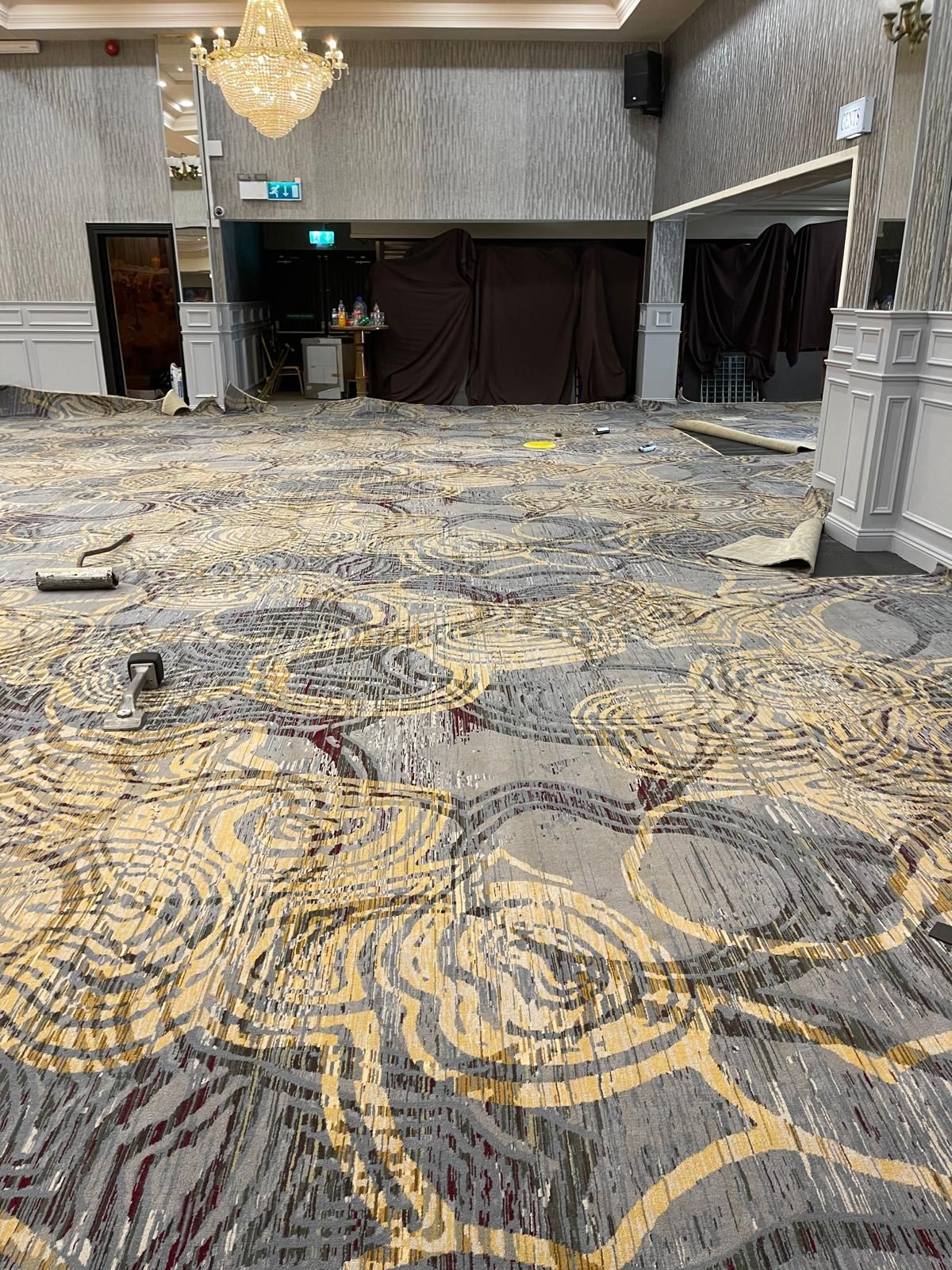 A large room with patterned carpet and damaged walls. A chandelier hangs from the ceiling.