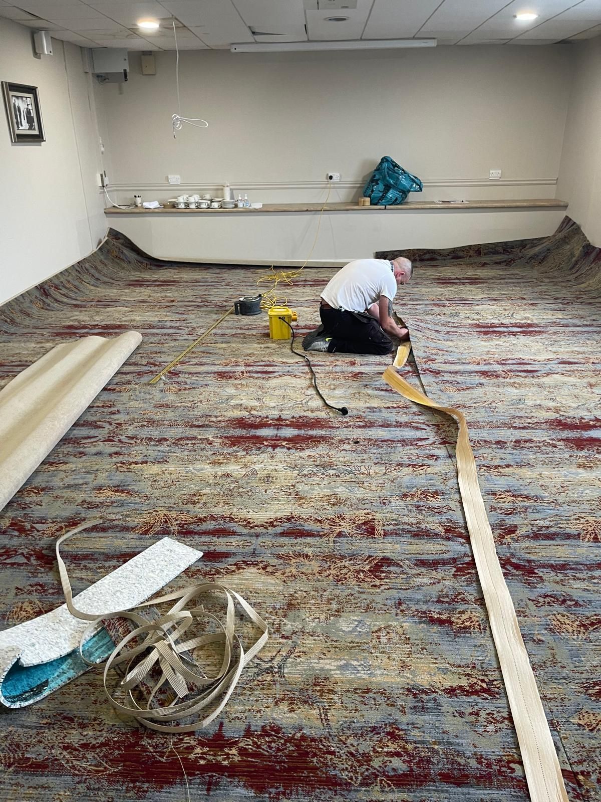 Person installing carpet in a room with light walls and a low counter.