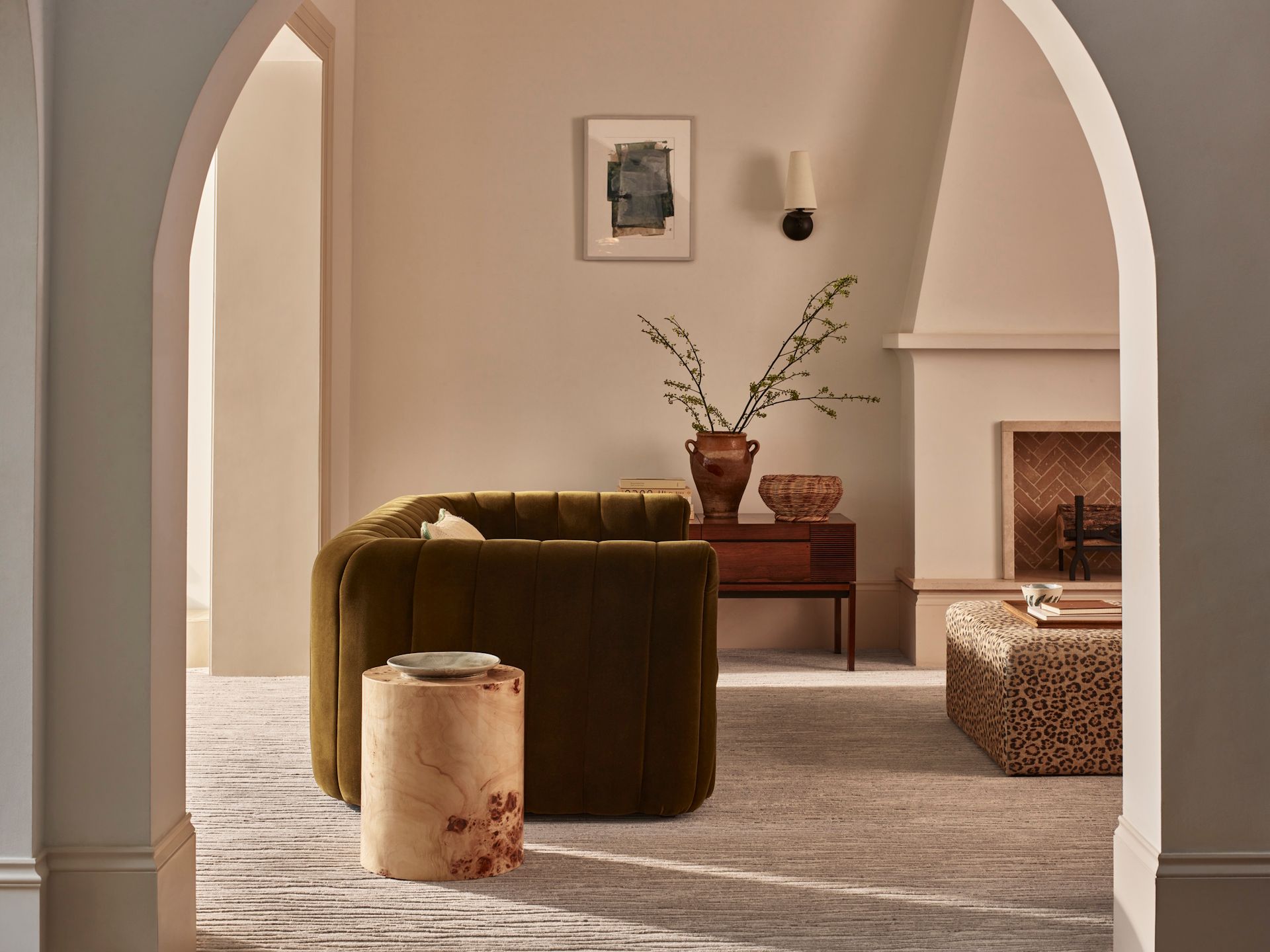 A stylish living room viewed through an archway, featuring a velvet sofa, a wooden side table, and a fireplace.