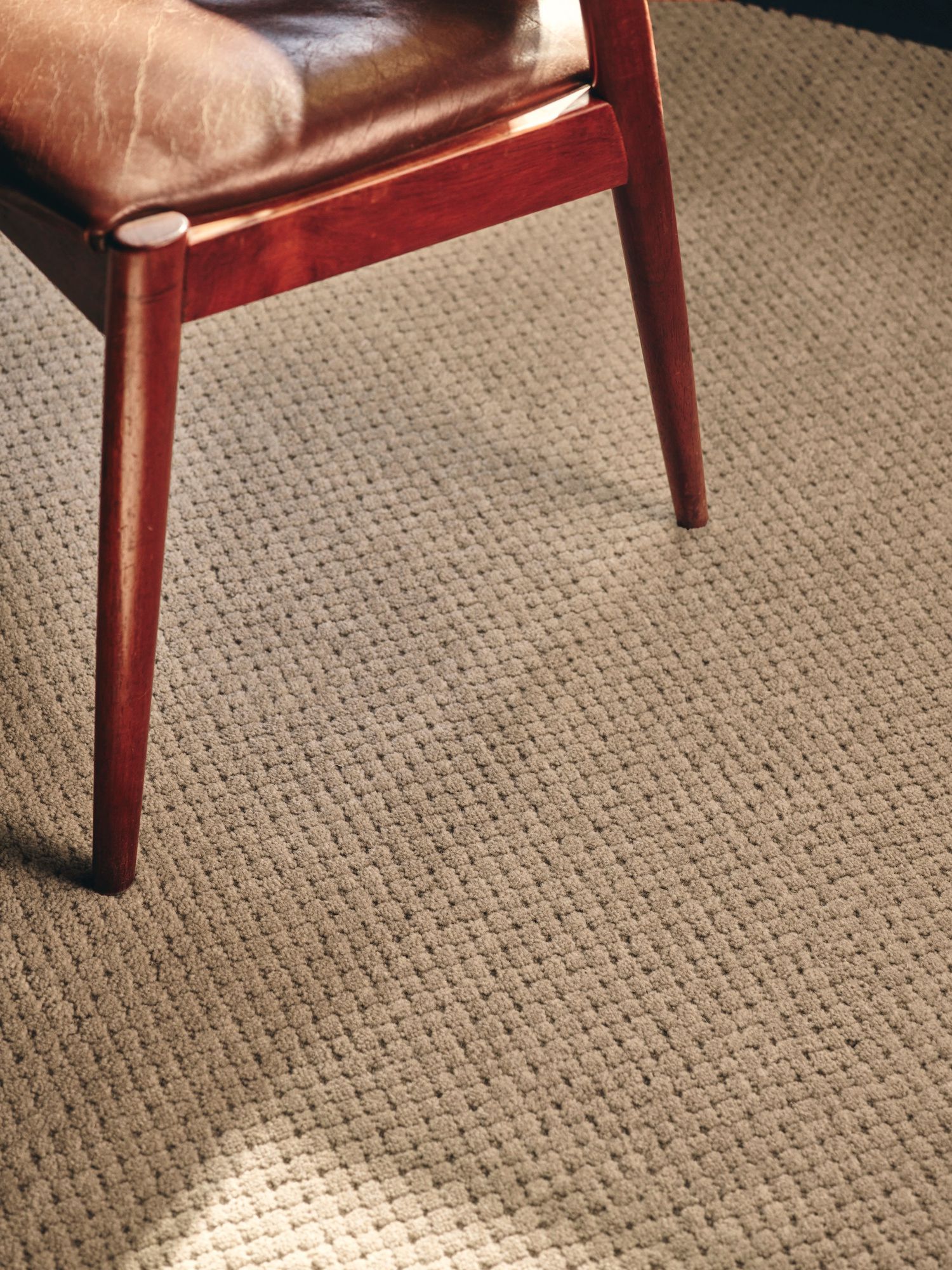 A close-up view of the legs of a wooden chair resting on a textured, light beige carpet.