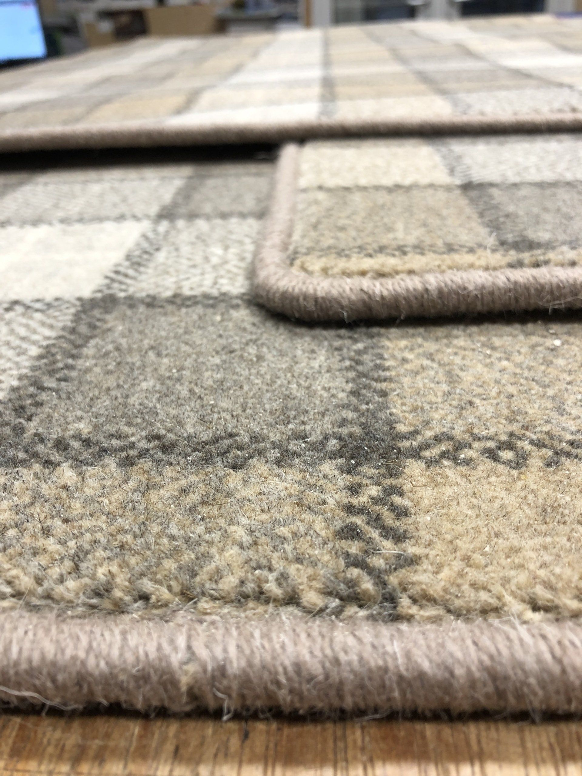 Close-up of a beige and gray plaid patterned rug with a contrasting border. The rug appears textured.