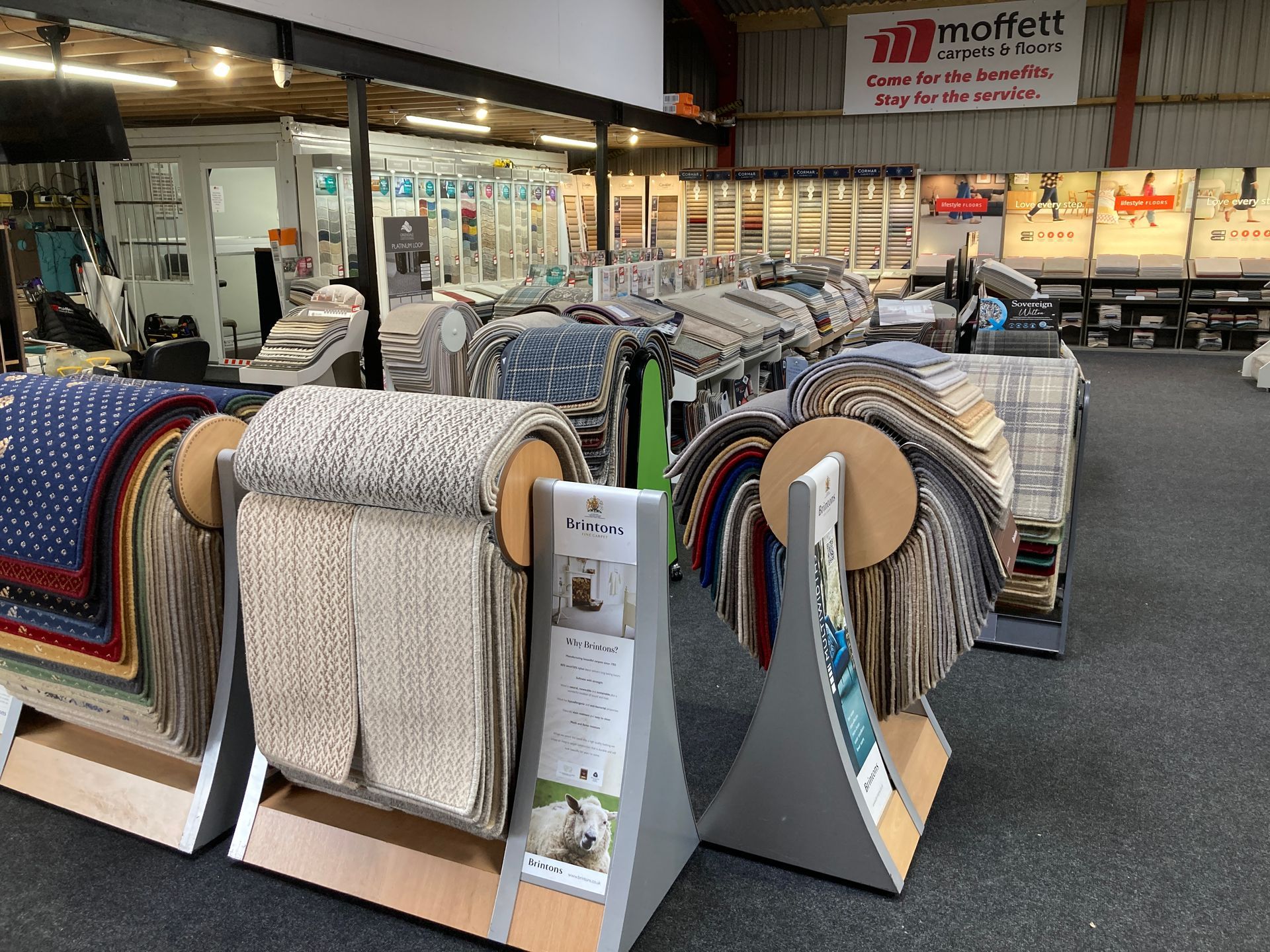 Interior showroom featuring rows of carpet sample racks with various textures and colors displayed on floor stands.