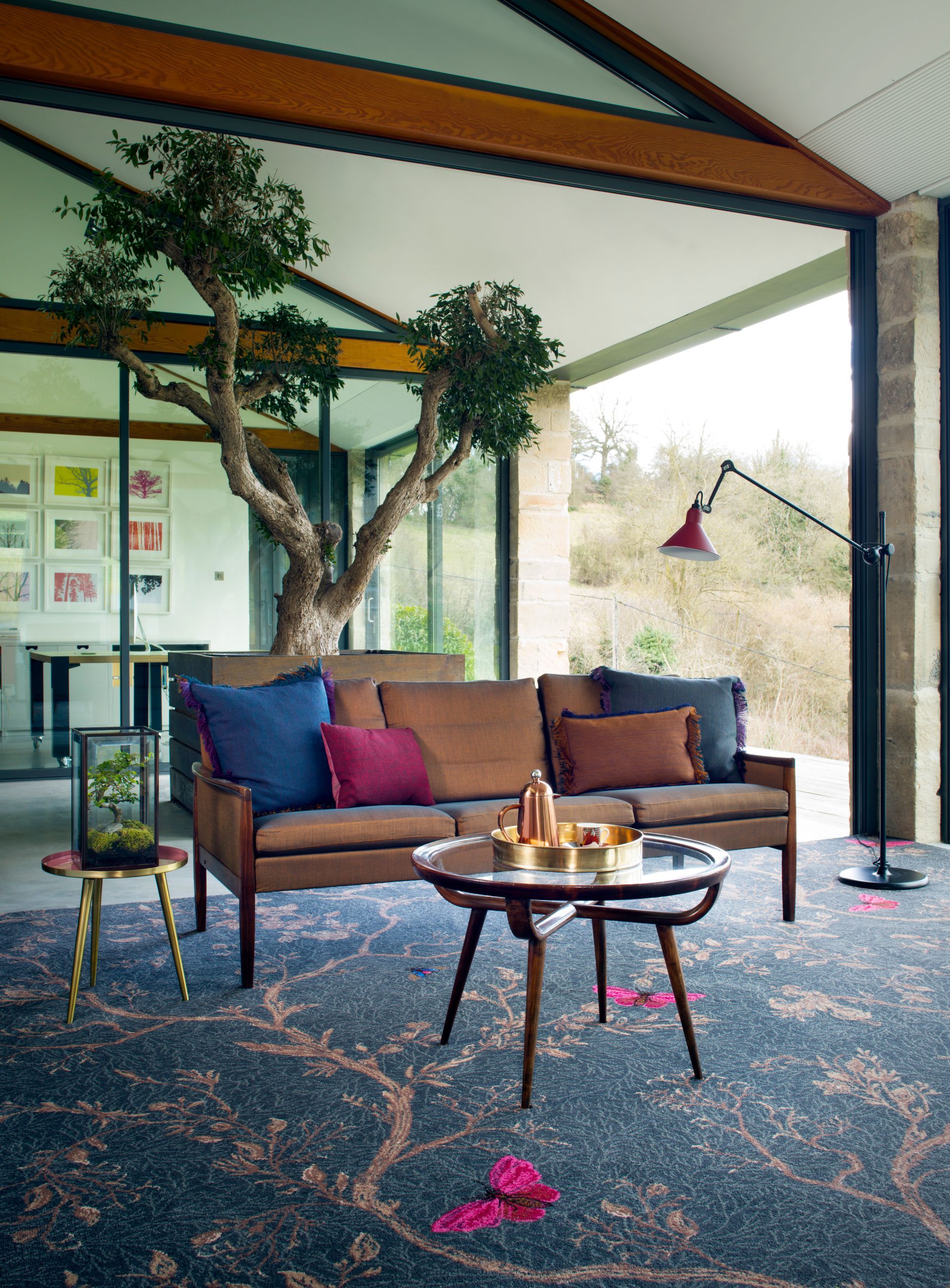 Modern living area with a brown sofa, a patterned rug, a round coffee table, and a tree growing inside the home.