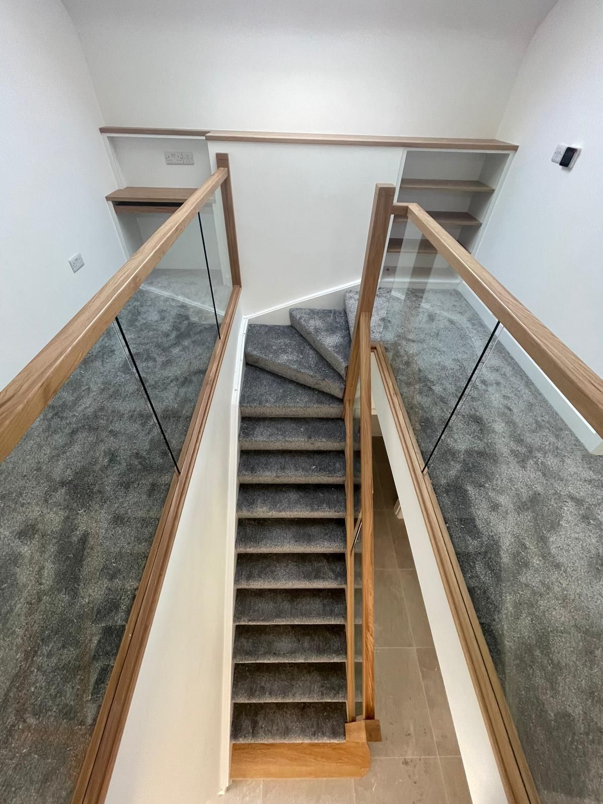 A staircase with a glass railing and carpeted steps in a house.