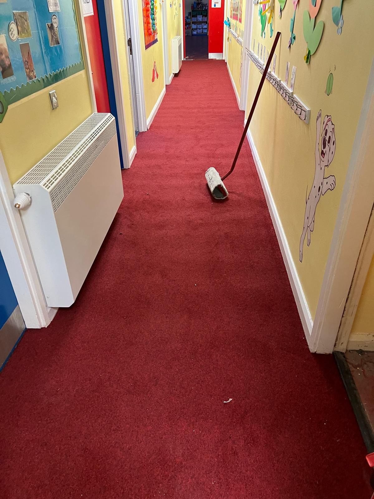 Red carpeted hallway with a heater, decorated walls, and a mop leaning against the wall.