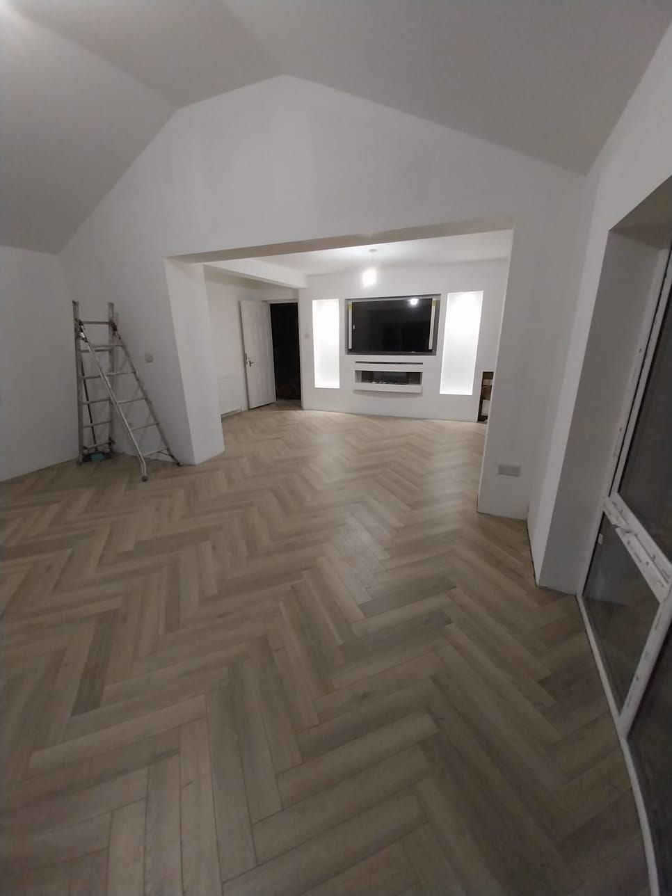A living room with a herringbone floor and a flat screen tv.