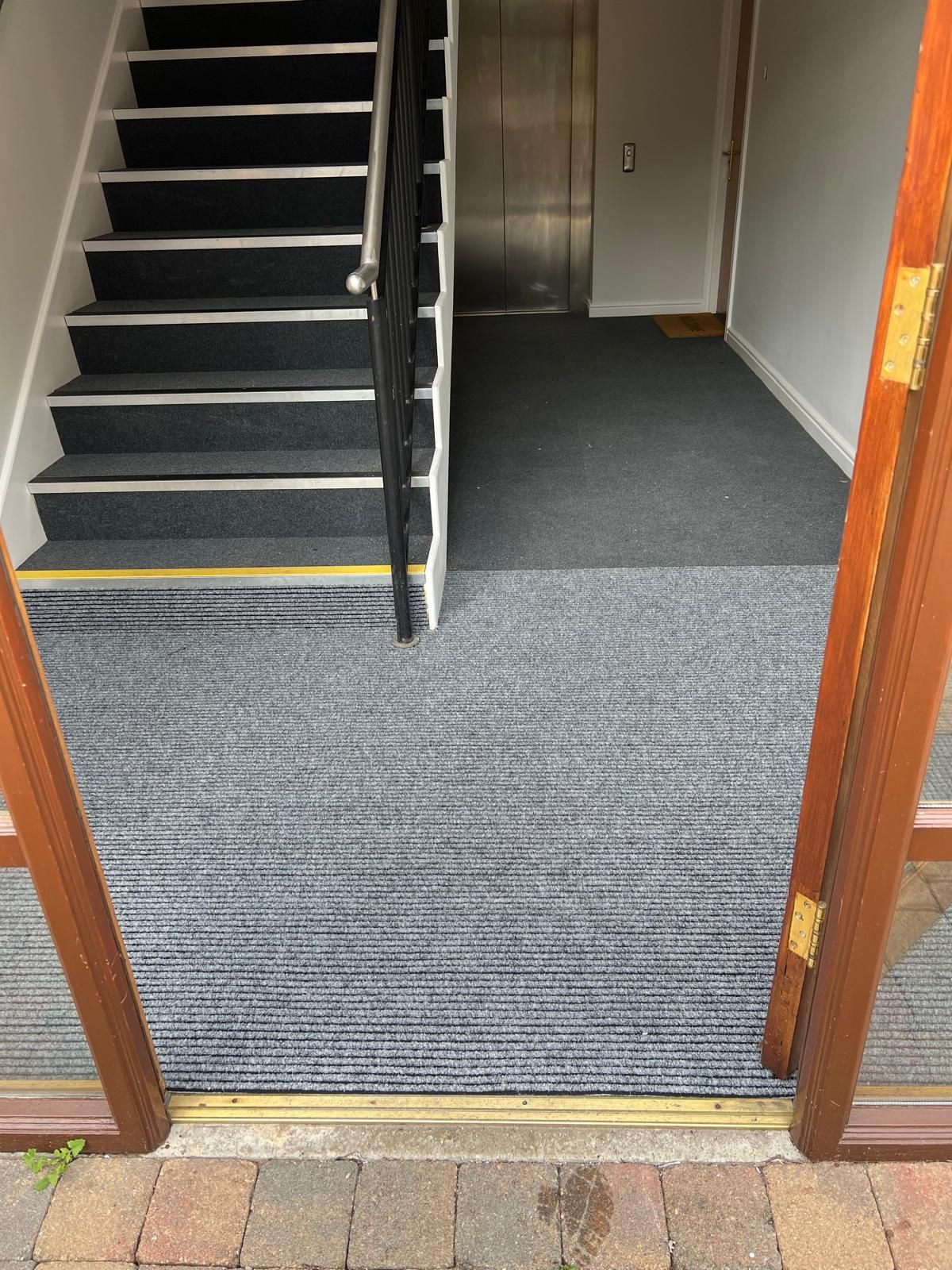 Entrance with open door, gray carpet, stairs, and elevator.
