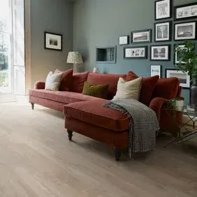 A living room with a red couch , ottoman , and pictures on the wall.