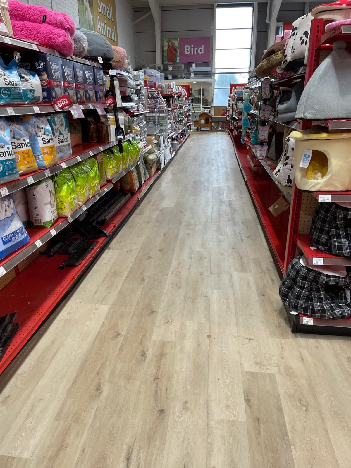 Interior of a pet store aisle, shelves stocked with pet supplies on either side, wooden floor.