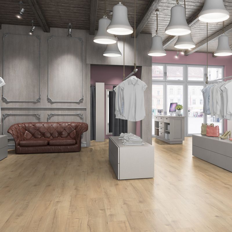 A retail clothing store interior with a leather sofa, hanging clothes, pendant lights, and light wood flooring.