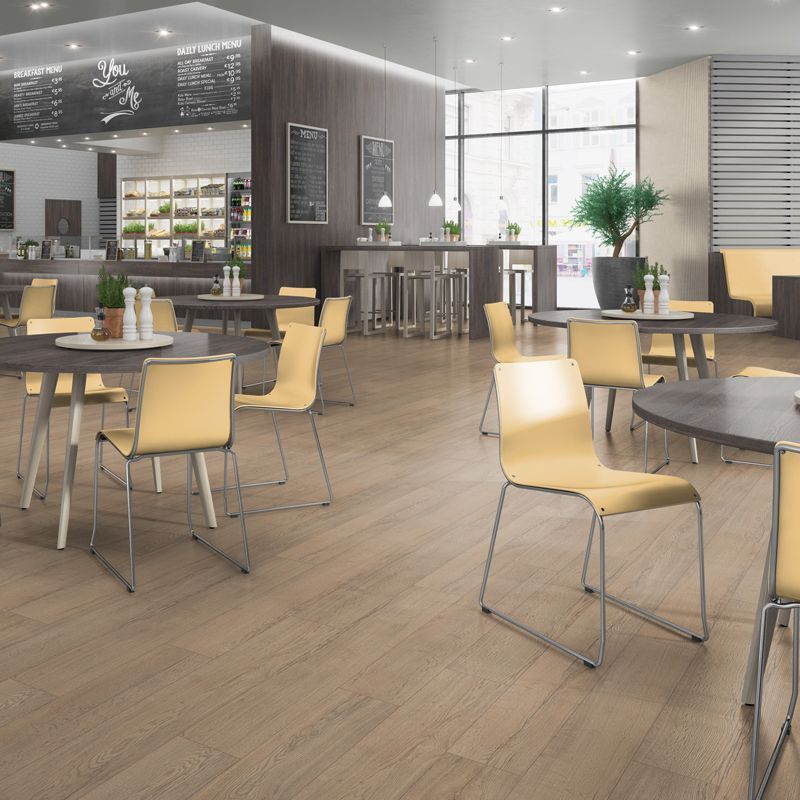 A bright, modern cafe interior with light wood flooring, several round tables, and beige chairs.