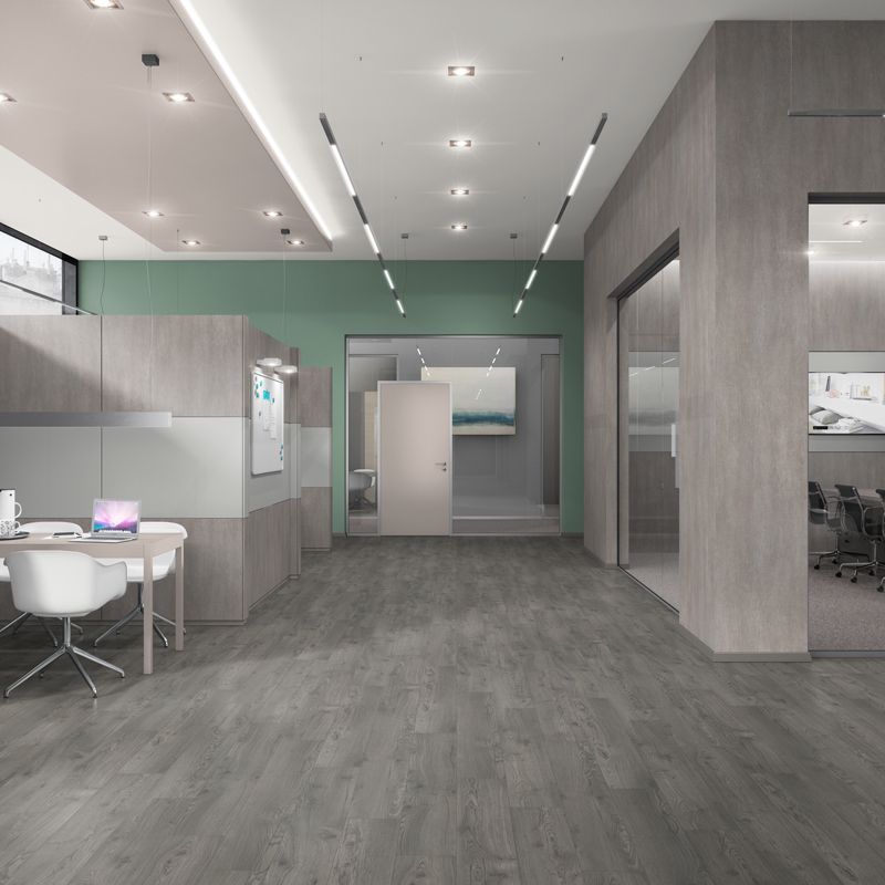 Modern office space with gray wood flooring, light wood partitions, green walls, and white chairs at a desk.