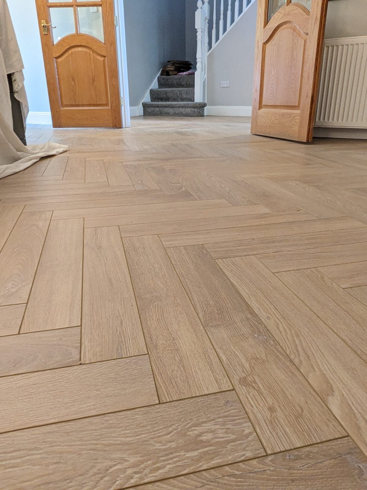 A wooden floor with a herringbone pattern and stairs in the background.