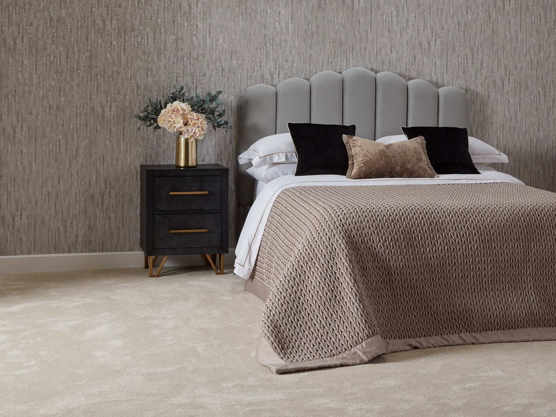 A bedroom with a bed , nightstand , and vase of flowers.
