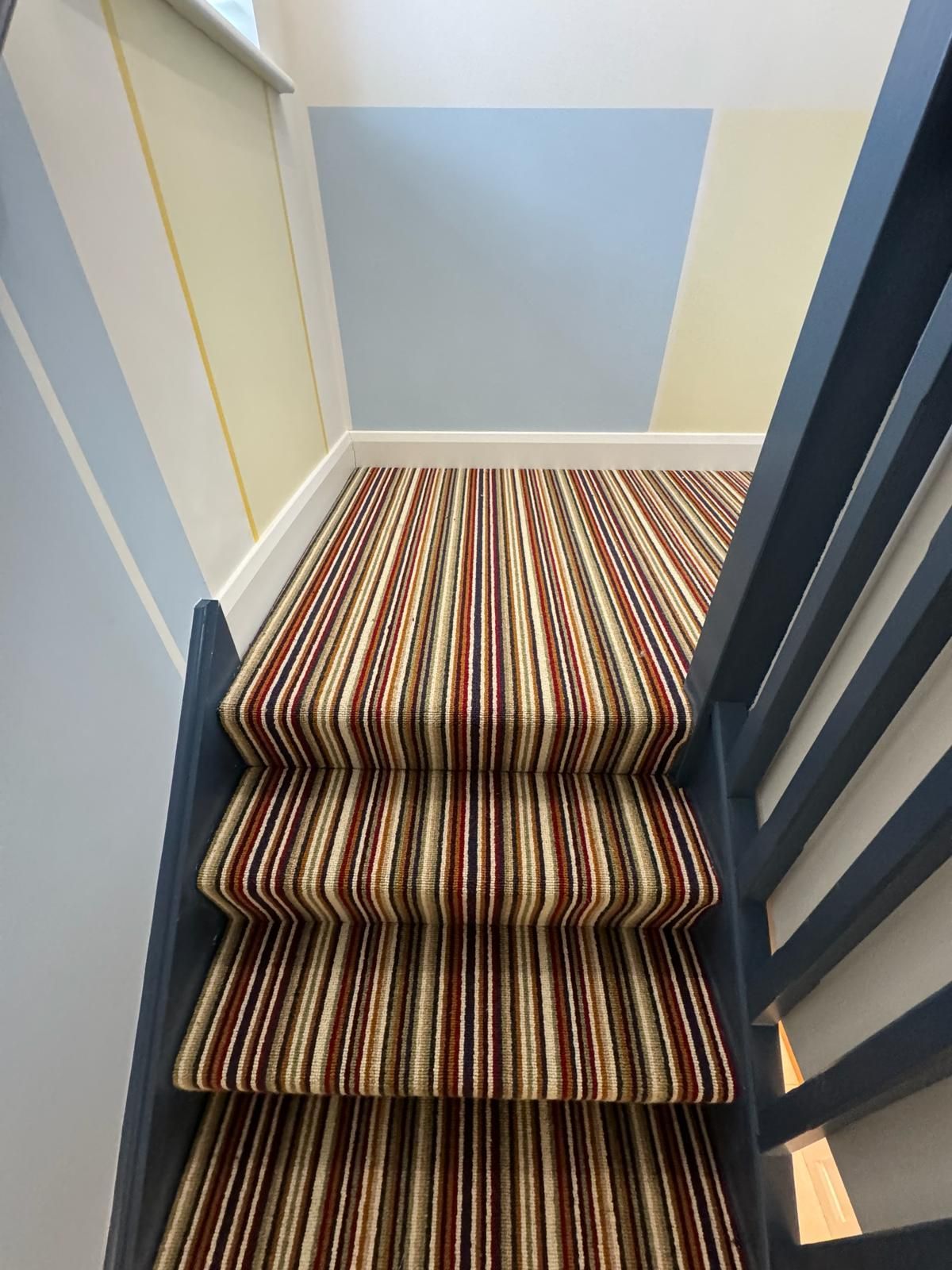 A staircase with a striped carpet and a blue railing.