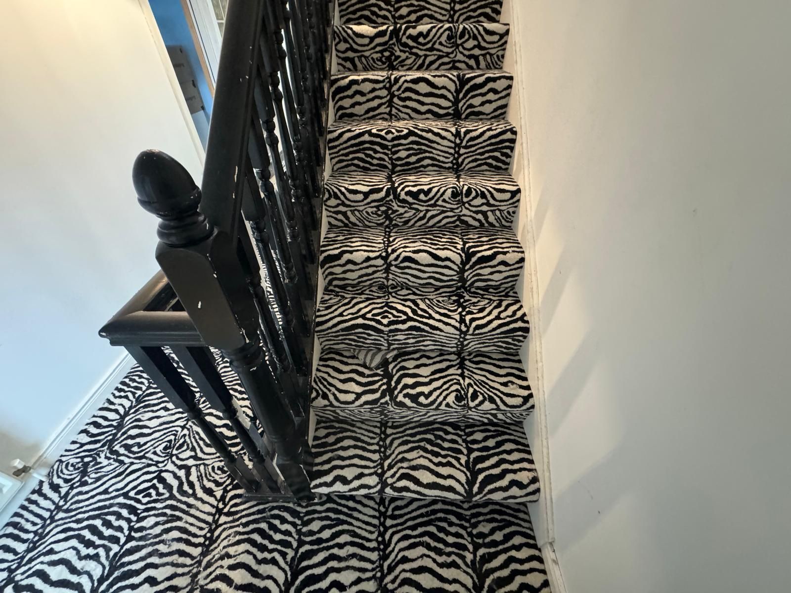 A staircase with a zebra print carpet and a black railing.
