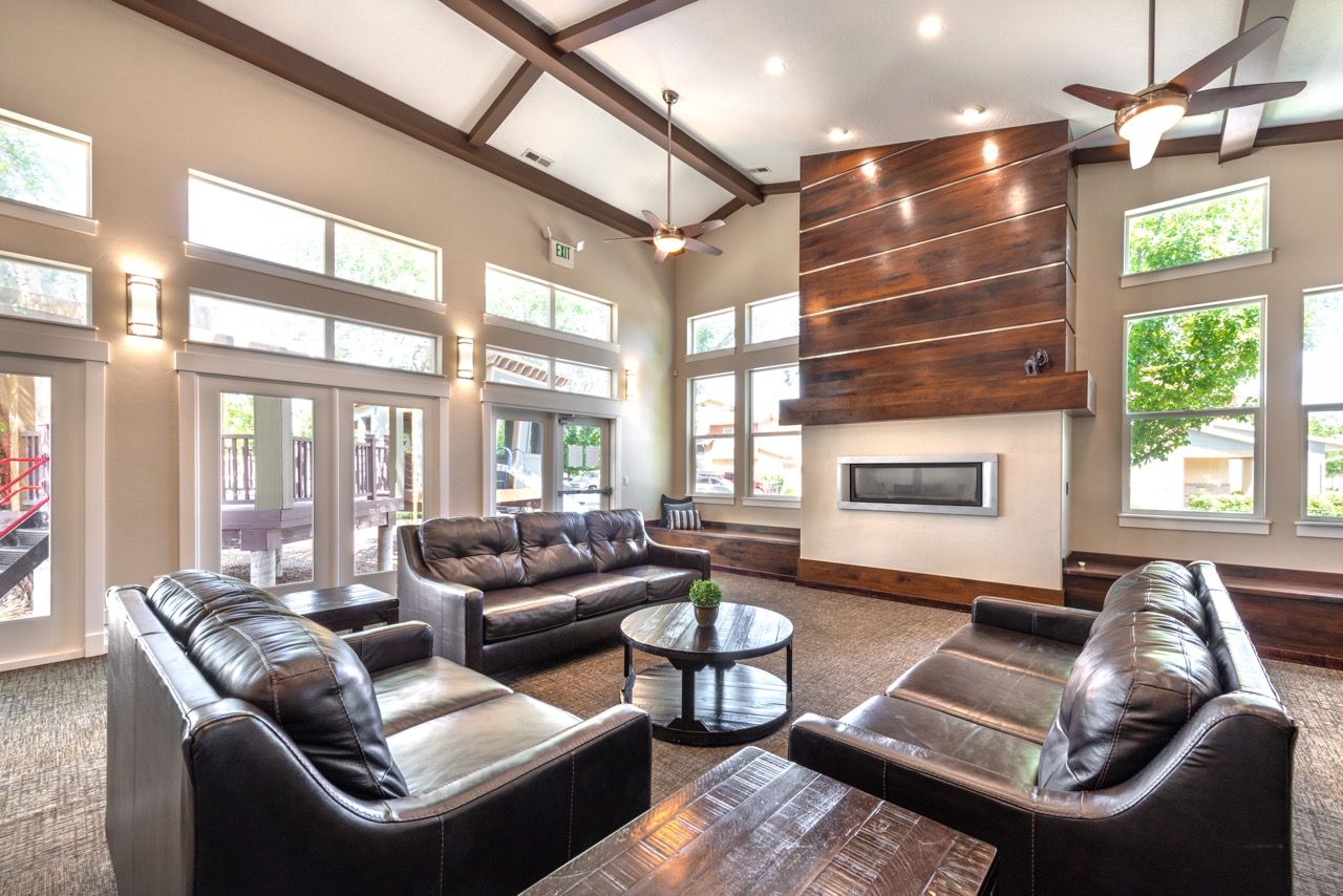 Interior community lounge with leather sofas, a modern fireplace, and large windows.
