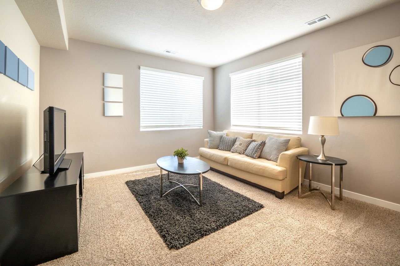 Bright living room with beige sofa, coffee table, TV, and large window blinds.