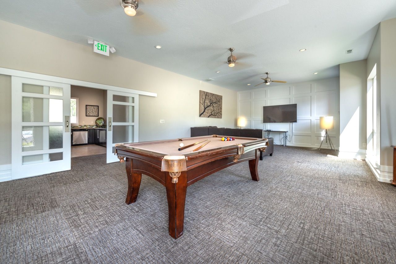 Community lounge with a pool table, sofa, TV, and ceiling fans.