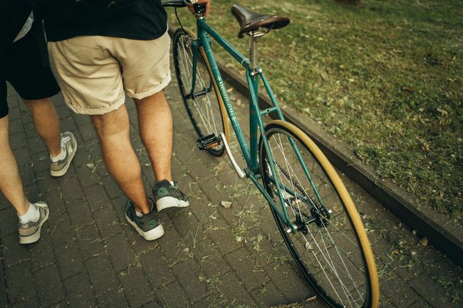 Two people walking on a paved path next to a teal bicycle, viewed from behind.