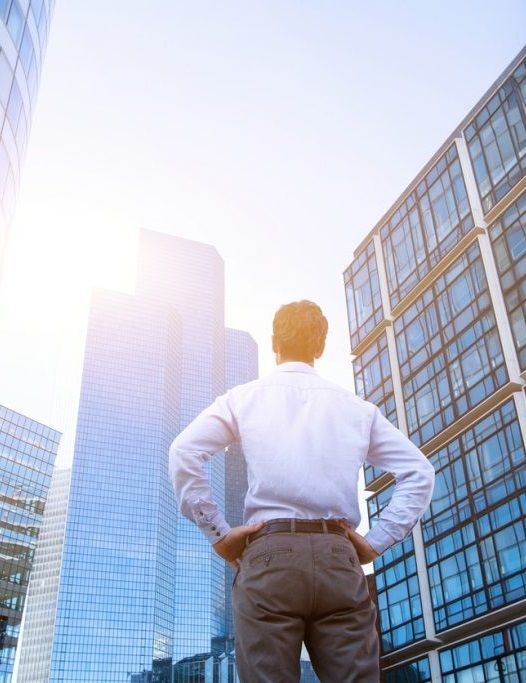 A man is standing in front of a tall building with his hands on his hips.