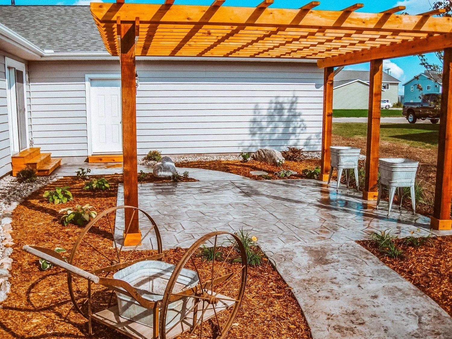 Wooden pergola over a stamped concrete patio, with chairs and landscaping.