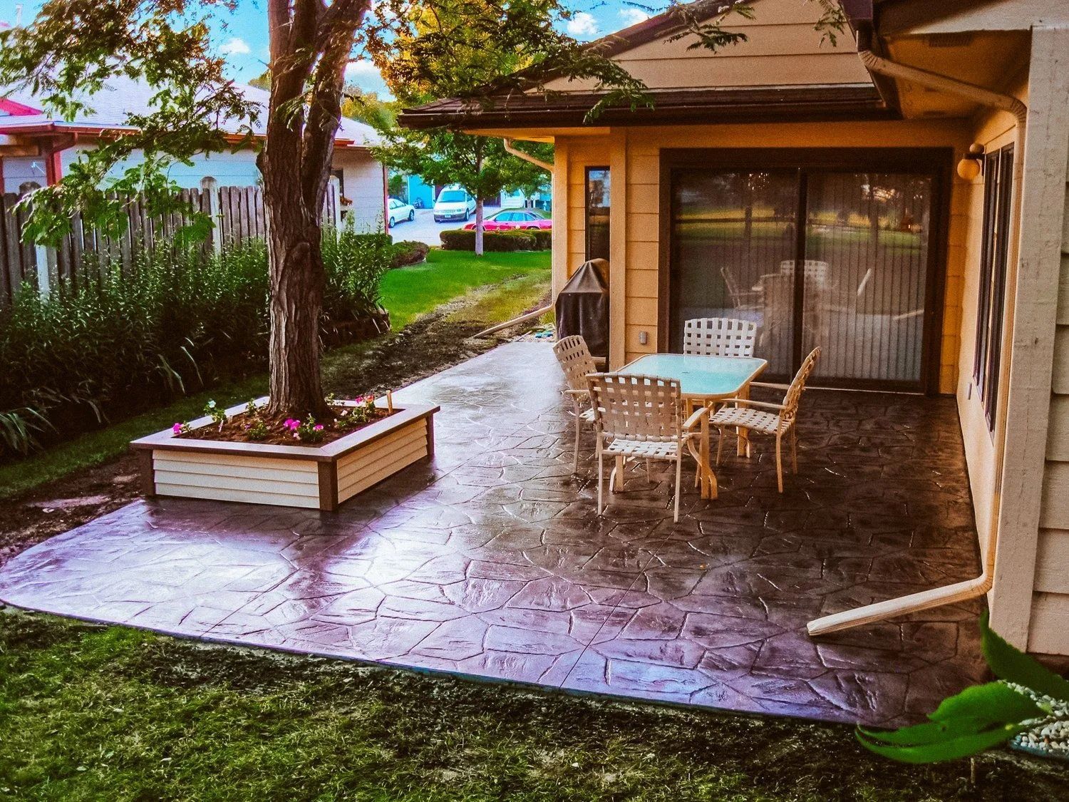 Patio with textured concrete, a tree planter, and outdoor dining set, next to a house.