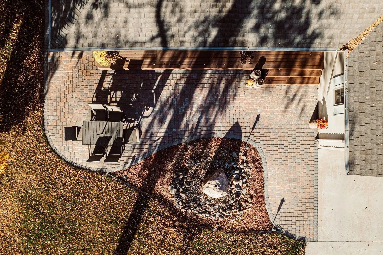 Overhead view of a brick patio with furniture, a rock feature, and a house exterior. Autumn leaves and shadows.