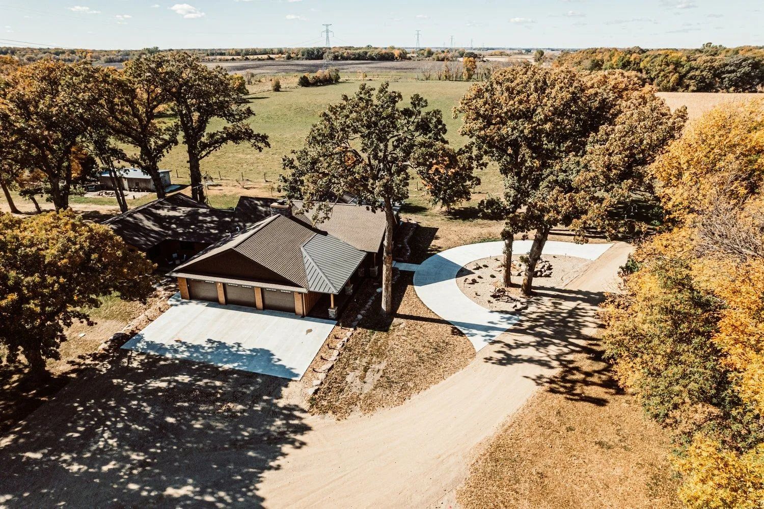 Aerial view of a house with a driveway and surrounding trees in a rural setting.