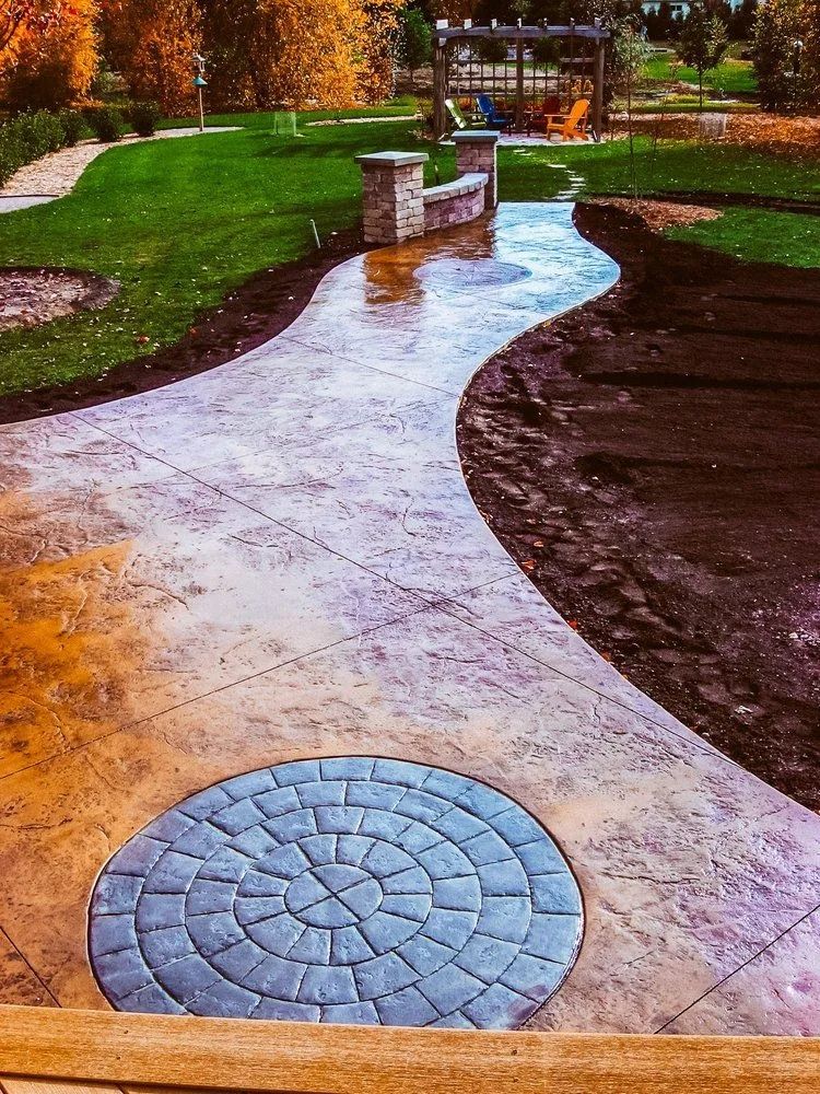 Stamped concrete pathway curves through a green park, leading to a wooden pergola in the distance.