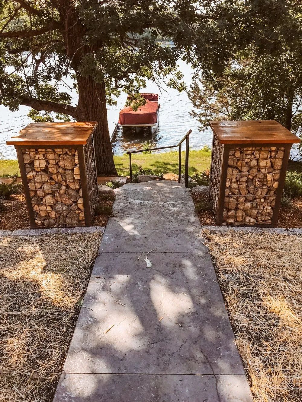 Pathway leading to a lake with a dock; stone columns with wooden tops flank the path.