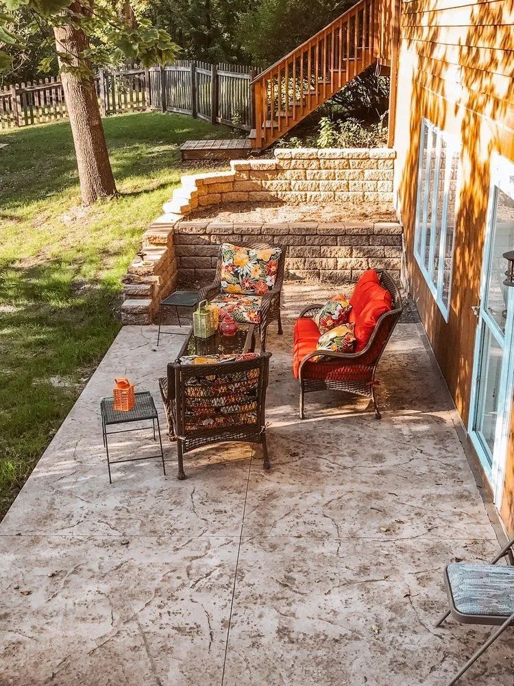 Patio with seating, stamped concrete, and tiered stone wall. Red and floral cushions.