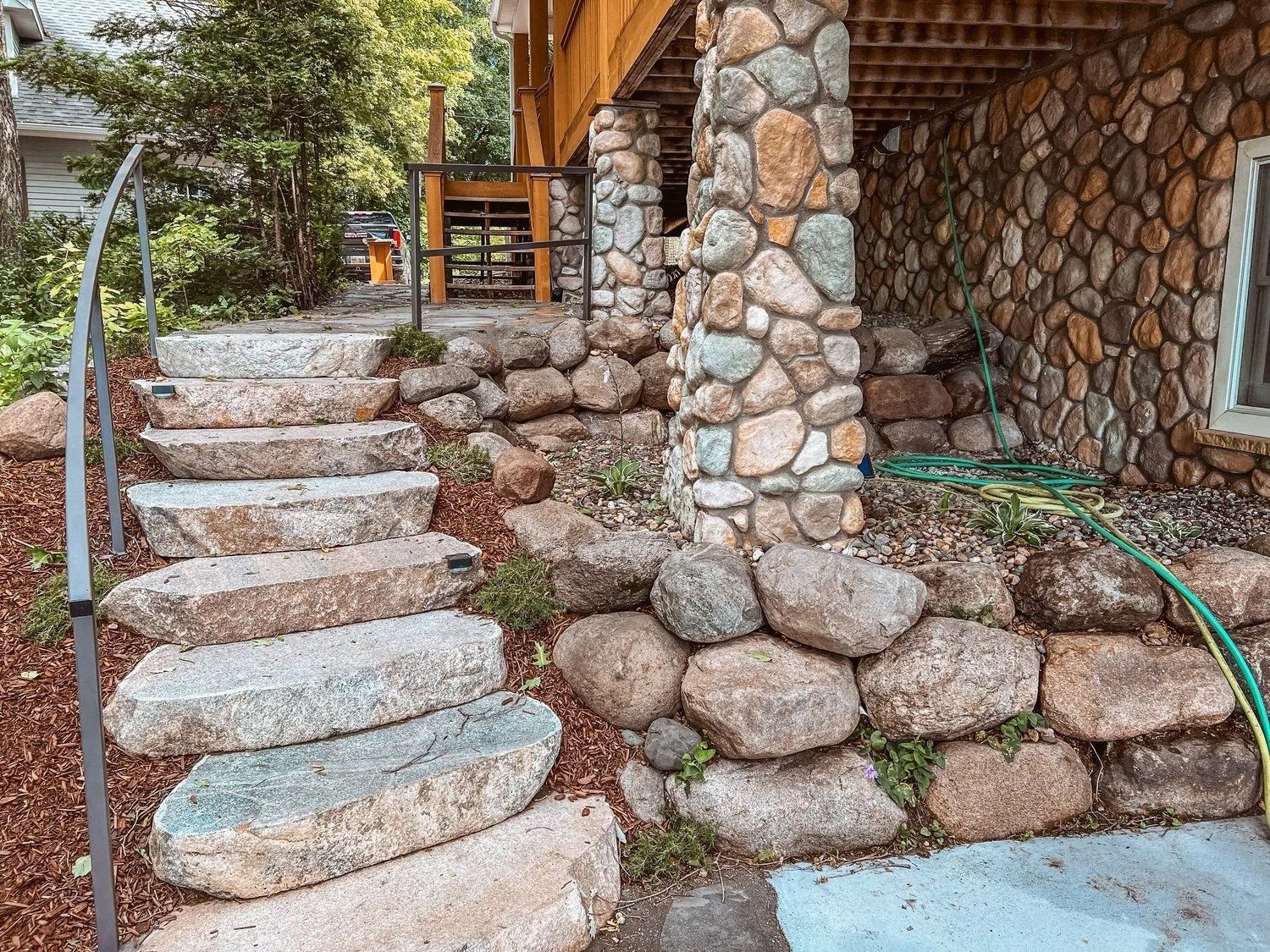 Stone steps leading up to a wooden deck, with stone pillars and retaining walls.