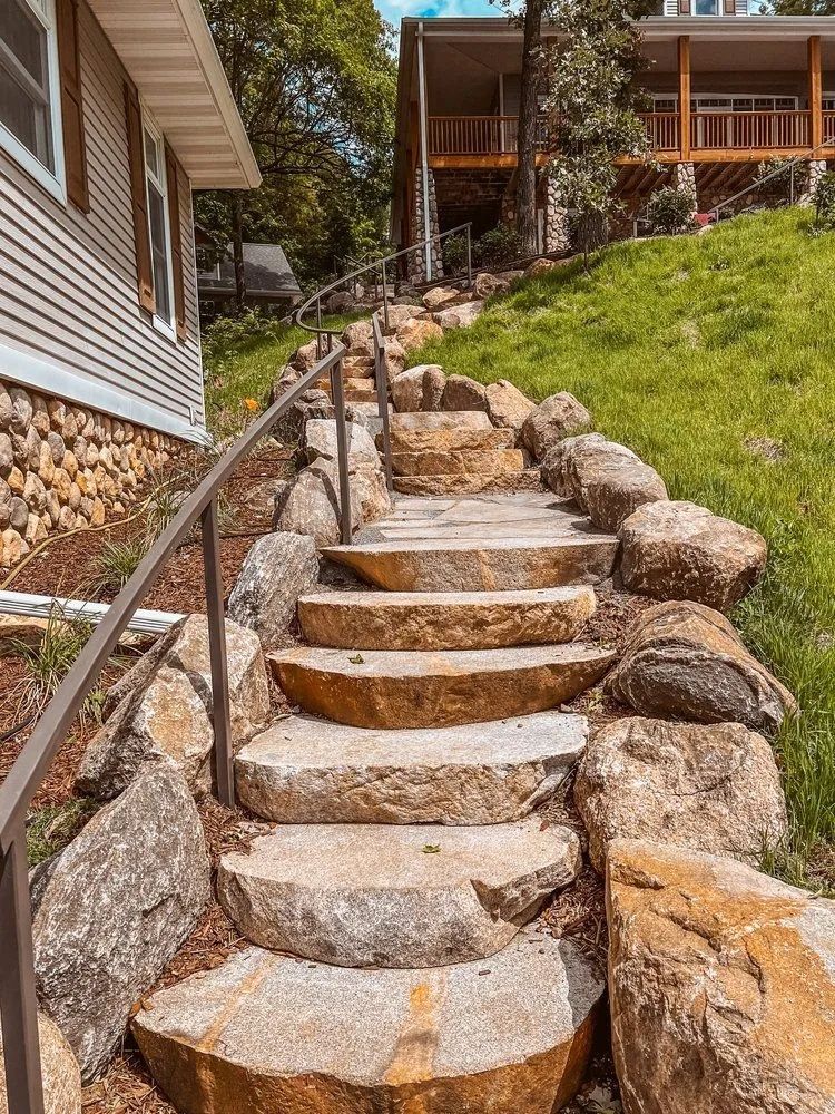 Stone steps with handrail leading up a grassy hill towards a house.