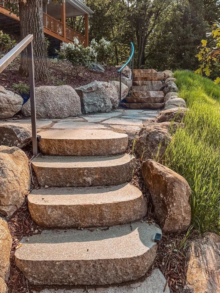 Stone steps lead up a hillside, surrounded by rocks and vegetation, towards a wooden structure.
