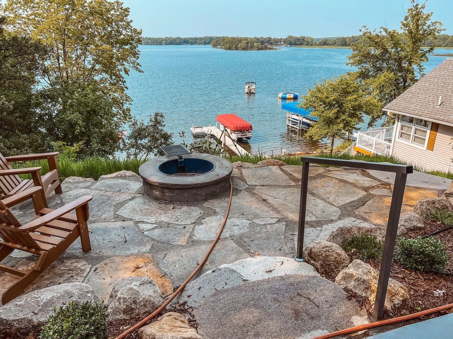 Patio overlooking a lake with a fire pit, wooden chairs, and docks.
