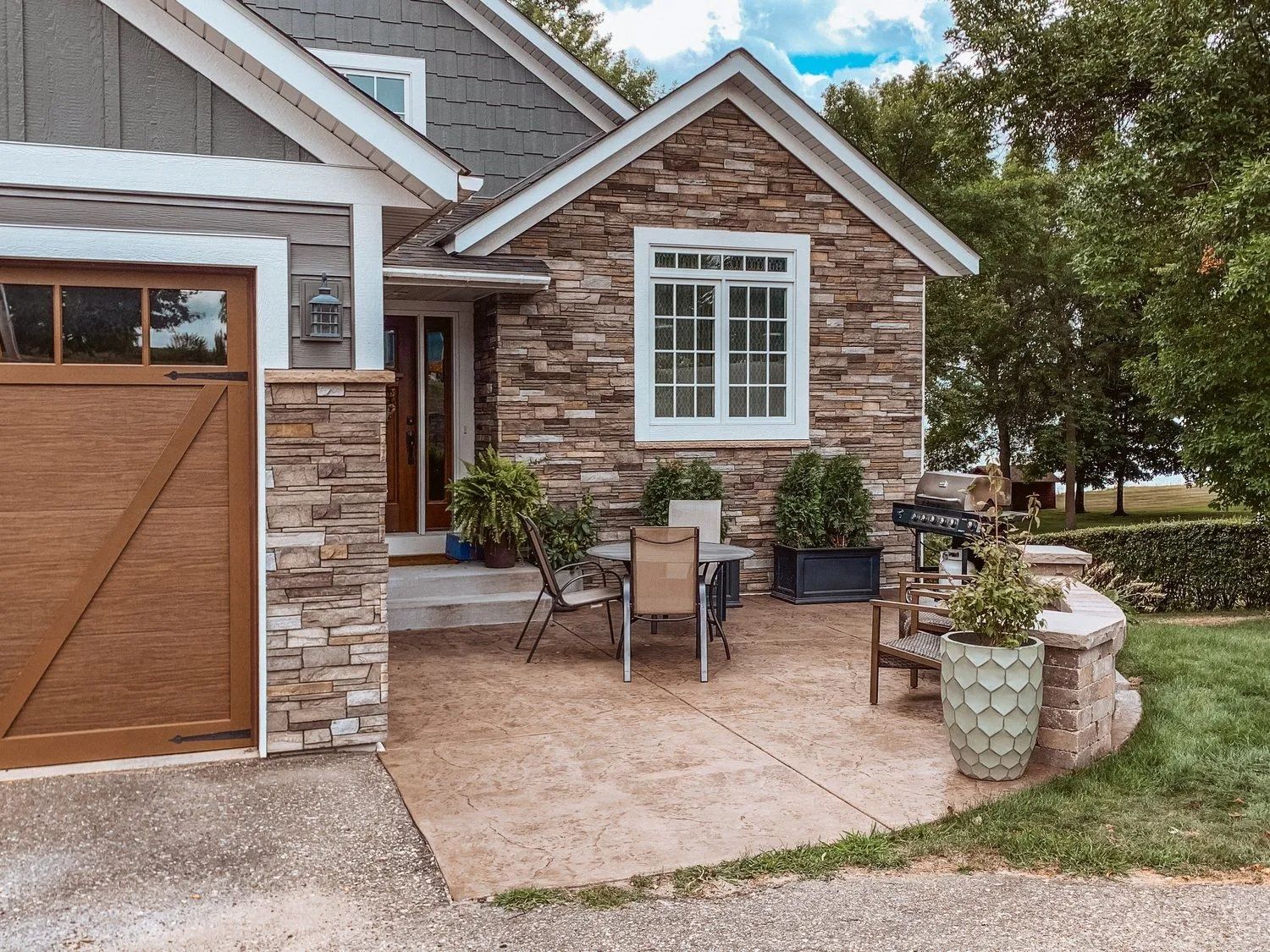House exterior with stone facade, garage door, patio with furniture, and landscaping.