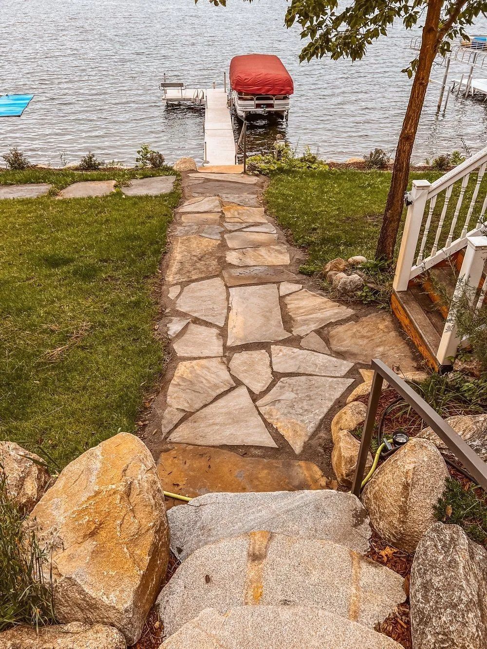 Stone pathway and steps leading to a dock with a boat lift on a lake.