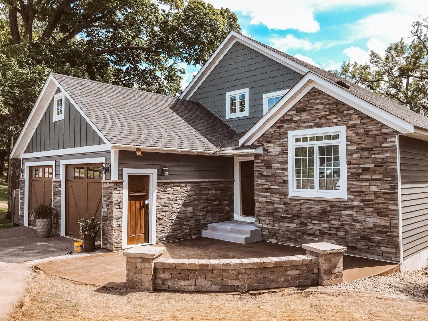 A house with stone facade, gray siding, brown garage doors, and a small front yard.