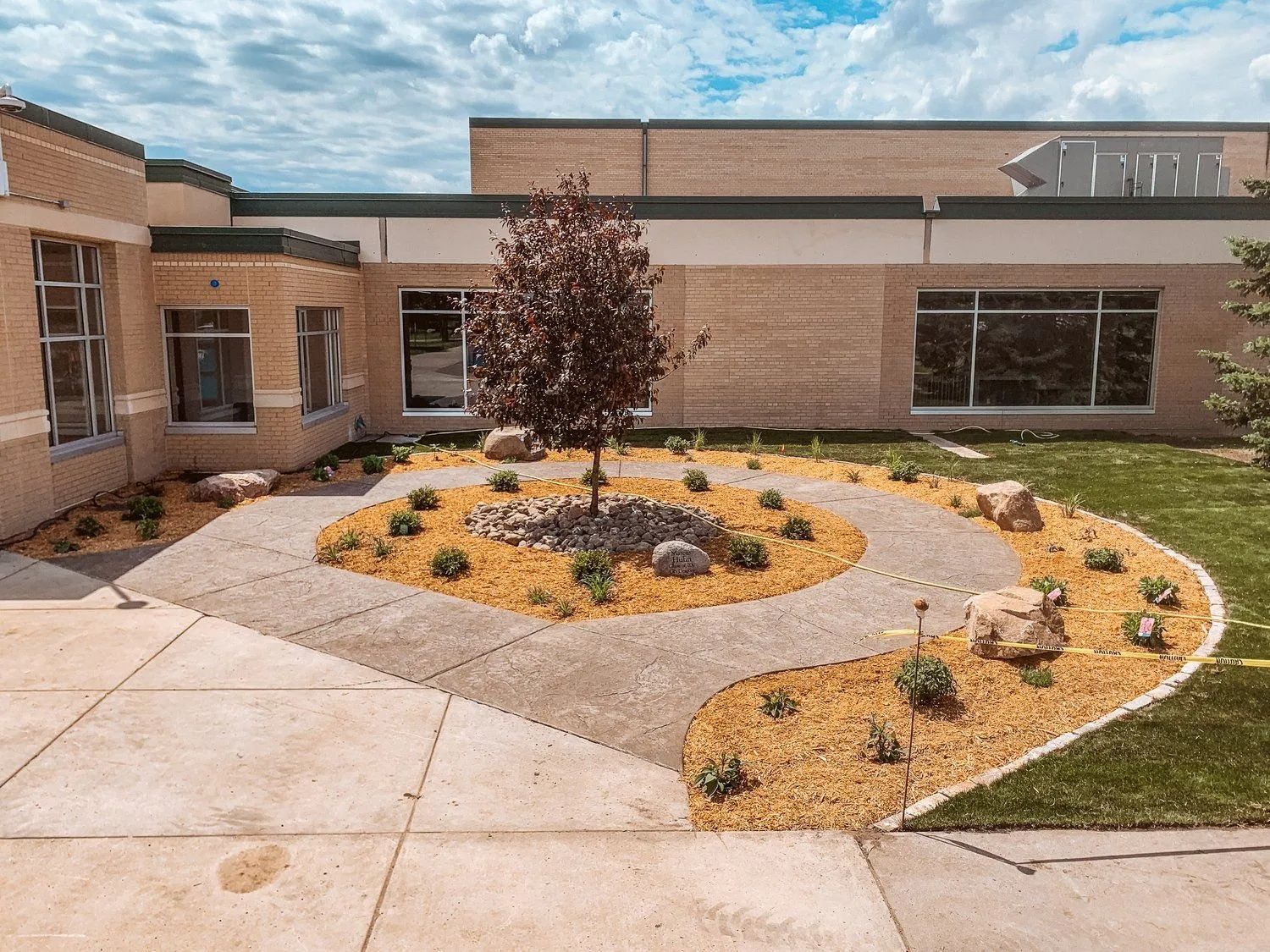 Landscaped area with tree, rocks, and mulch in front of a building with windows.