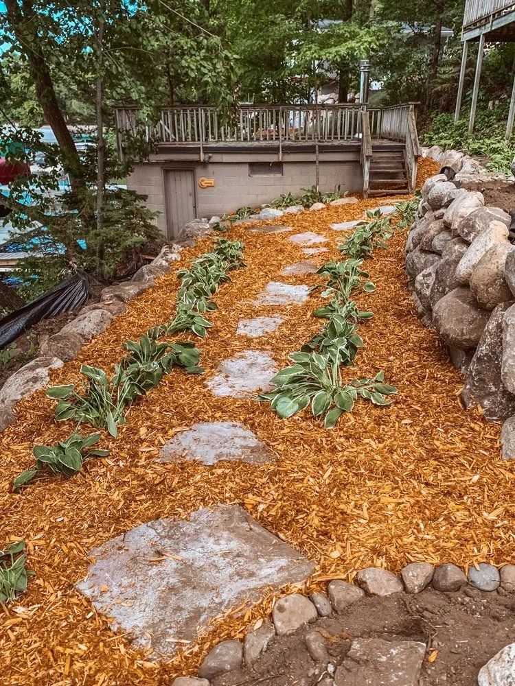 Stone path through a terraced garden with wood chips, plants, and a retaining wall near a wooden deck.