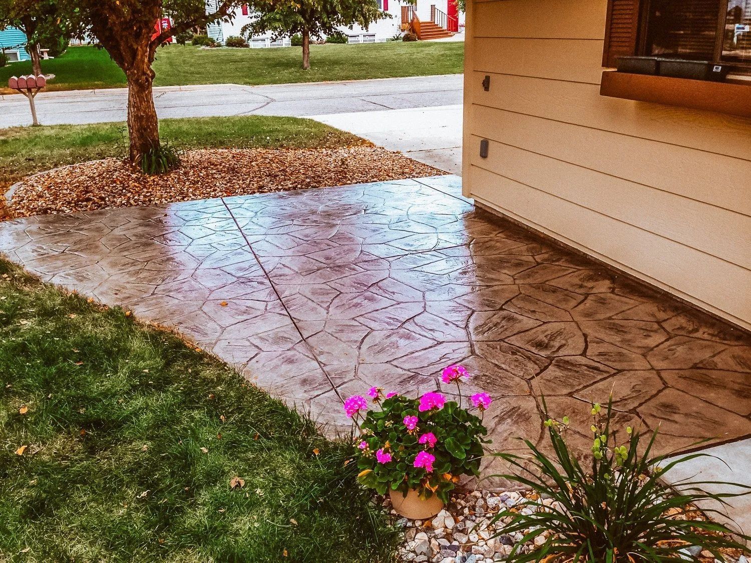 Stamped concrete walkway next to a beige building with a small flower pot and tree.