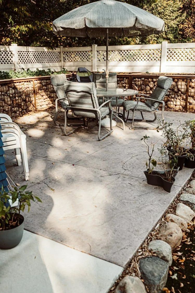 Patio with furniture, umbrella, and decorative stone walls and edge in a backyard setting.