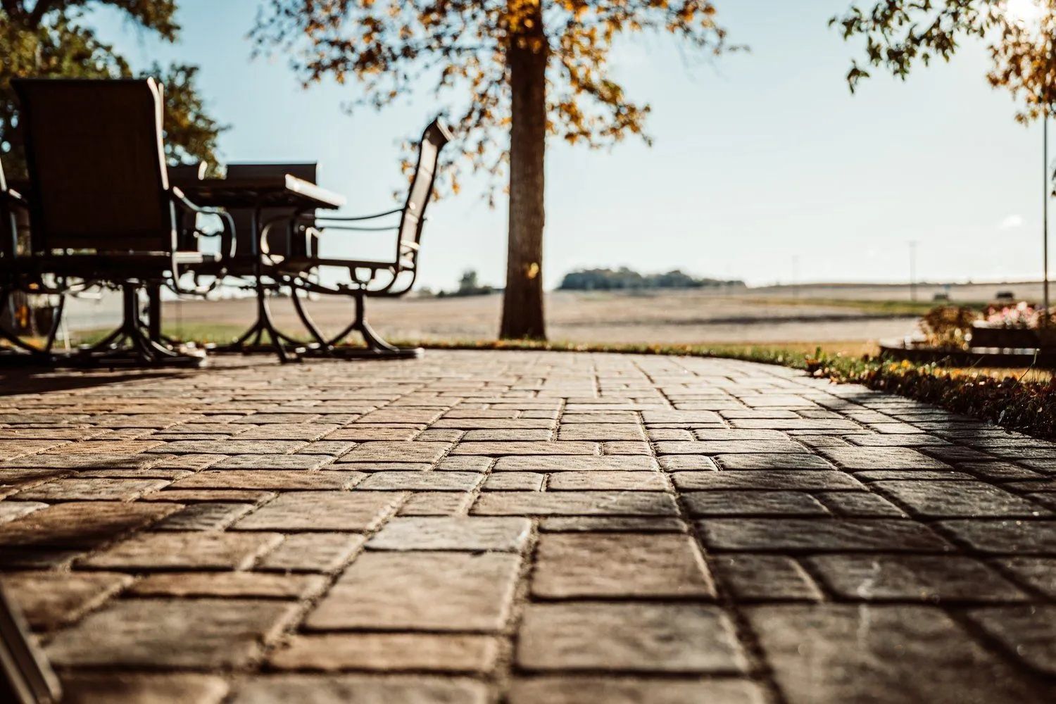 Paver patio with wrought iron table and chairs, sunlight, blurred fields and tree.