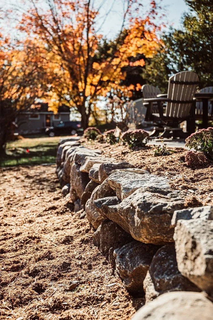 Stone retaining wall with orange fall foliage in background.