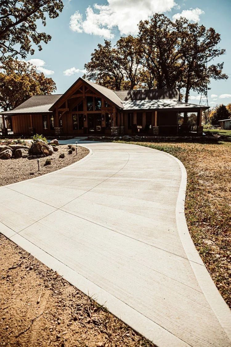 Concrete driveway curving to a wooden lodge-style house on a sunny day.