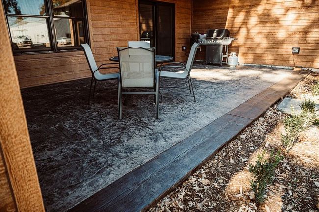 Patio furniture and grill sitting on top of a dark gray patio concrete stamping.