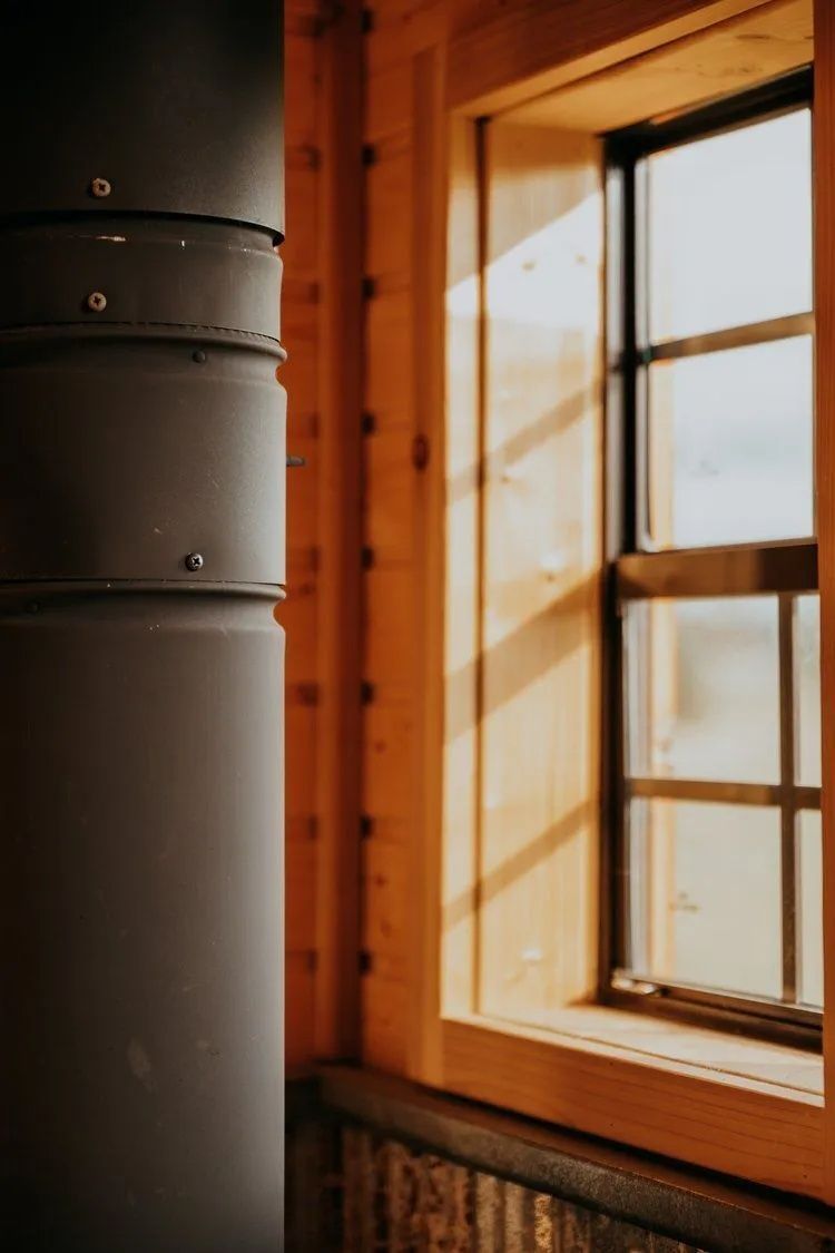 Black stove pipe and wooden window frame; warm light streams in.