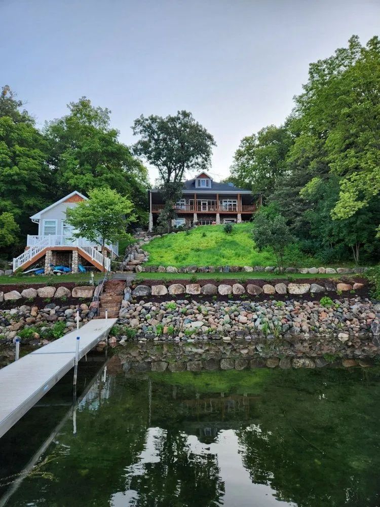 Lakeside houses on a hill, with a dock and green water.